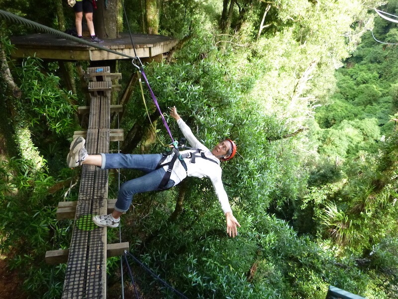 Writer hanging by ropes off a wooden bridge on native tree walk in Rotorua, NZ.